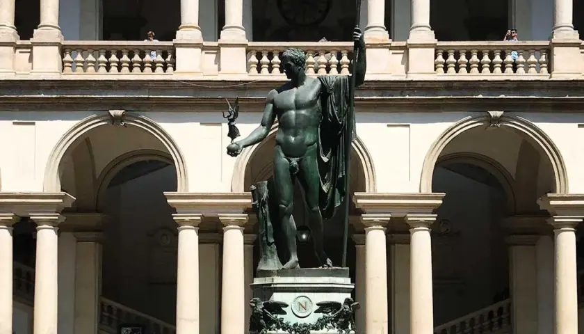 Wielki posąg w centrum dziedzińca Pinacoteca. Nad nim arkady i balustrada, z której obserwują ludzie.