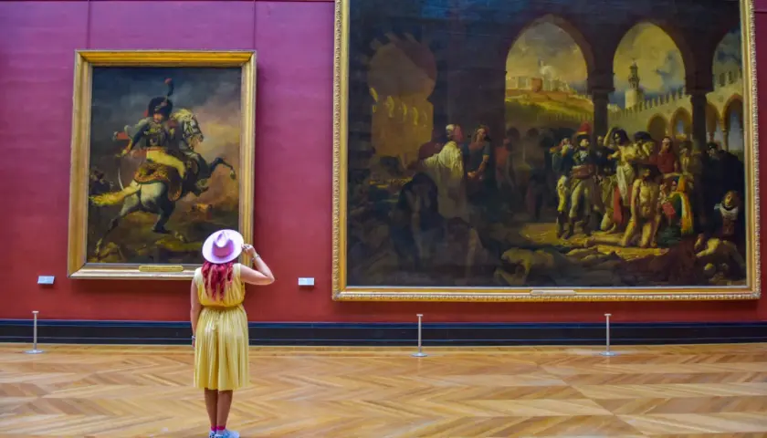 Kobieta w różowym kapeluszu podziwia obrazy w najwiekszym muzeum świata.