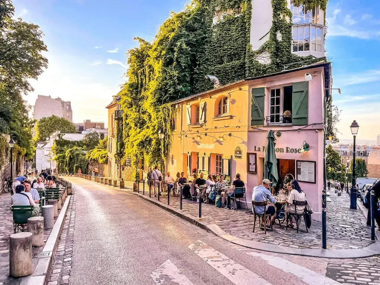 Ulica Montmartre w Paryżu z kawiarnią La Maison Rose i ludźmi siedzącymi przy stolikach.
