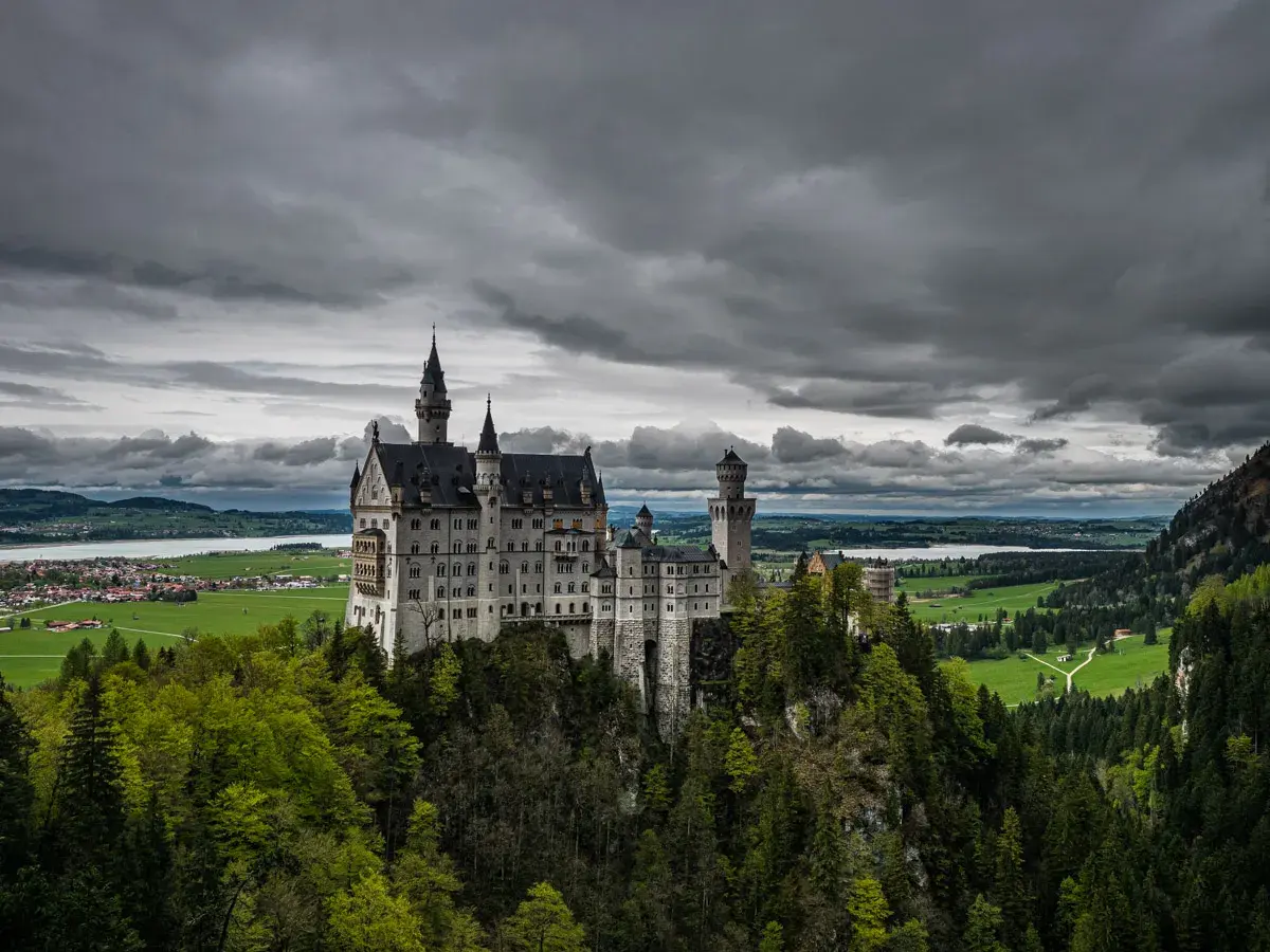 Bajkowy zamek Disneya w Niemczech, Neuschwanstein, wznosi się na skalistym wzgórzu, otoczony zielonymi lasami i malowniczym jeziorem.