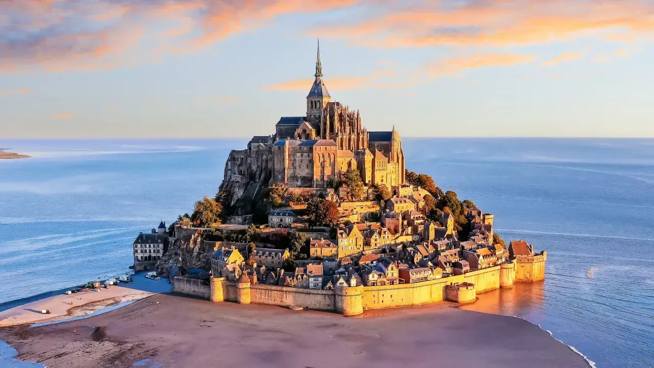 Opactwo Mont Saint-Michel na skalistej wyspie otoczonej wodą, o zachodzie słońca.