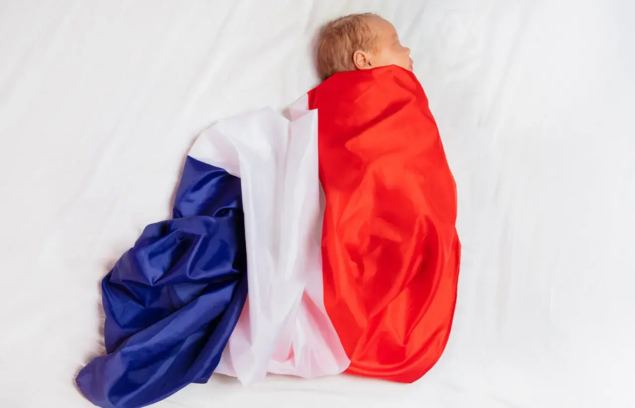 Noworodek owinięty w flagę Francji na białym tle.