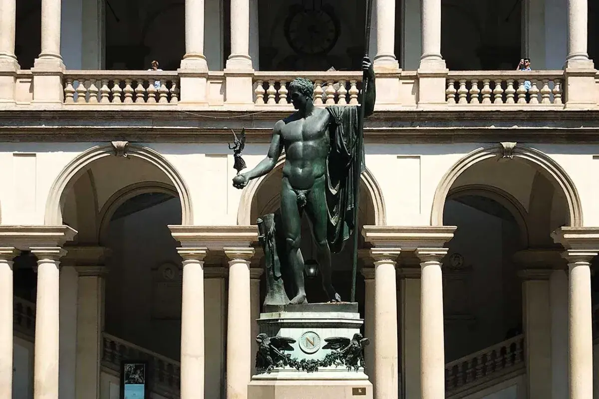 Wielki posąg w centrum dziedzińca Pinacoteca. Nad nim arkady i balustrada, z której obserwują ludzie.