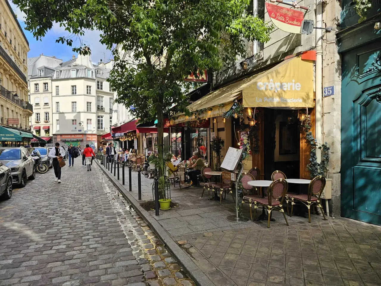 Ulica w dzielnicy łacińskiej Paryża z kawiarnią "La Petite Boulangerie" i brukowanym chodnikiem.