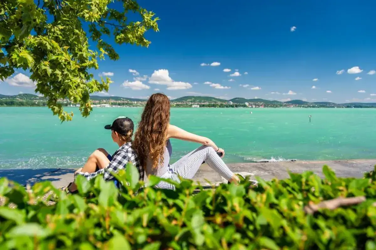 Dzieci odpoczywają na plaży Balaton, podziwiając turkusową wodę i zielone wzgórza w oddali.