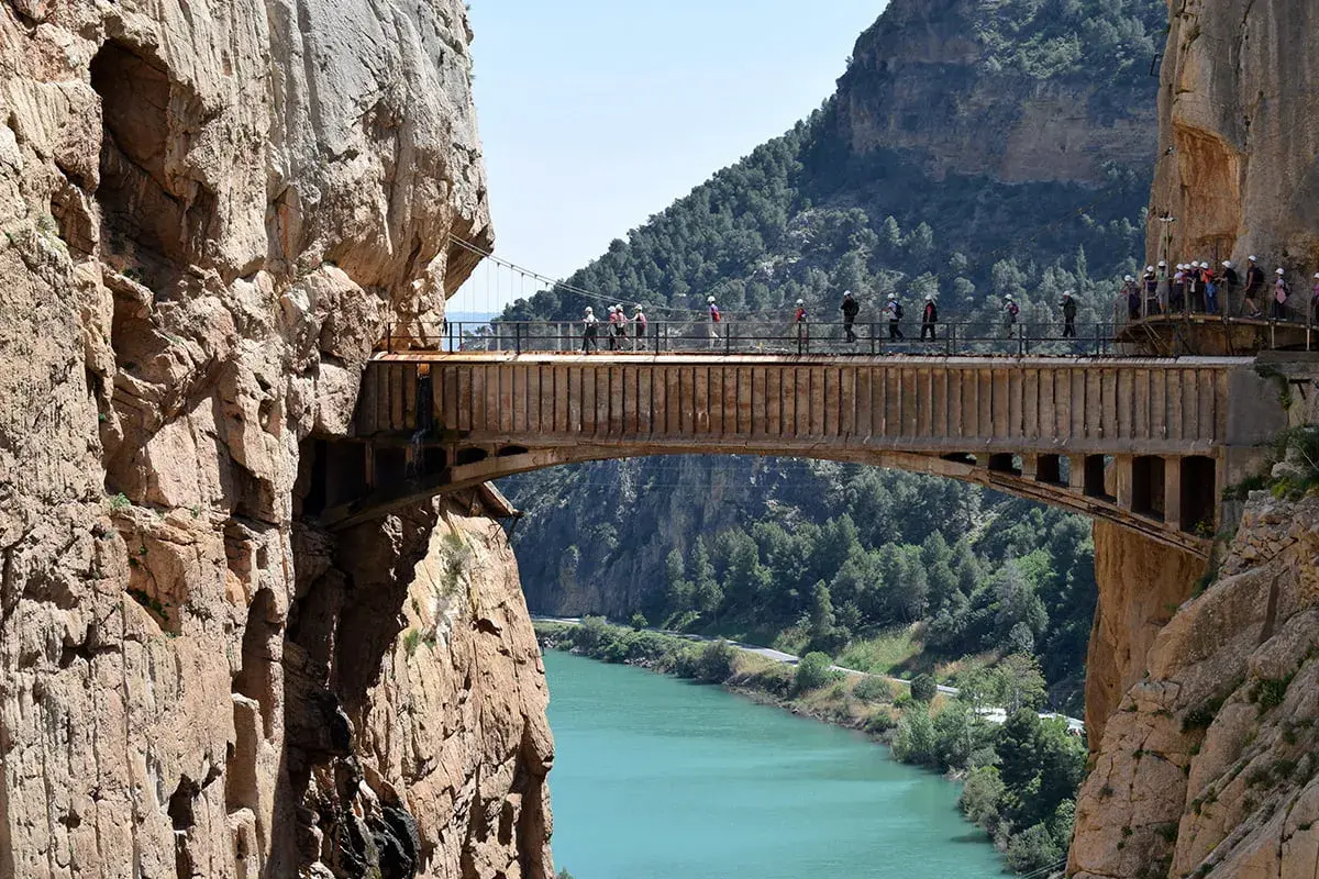 Spacerzy po wąwozie El Caminito del Rey, atrakcji, z której słynie Malaga. Widok na most nad turkusową rzeką.