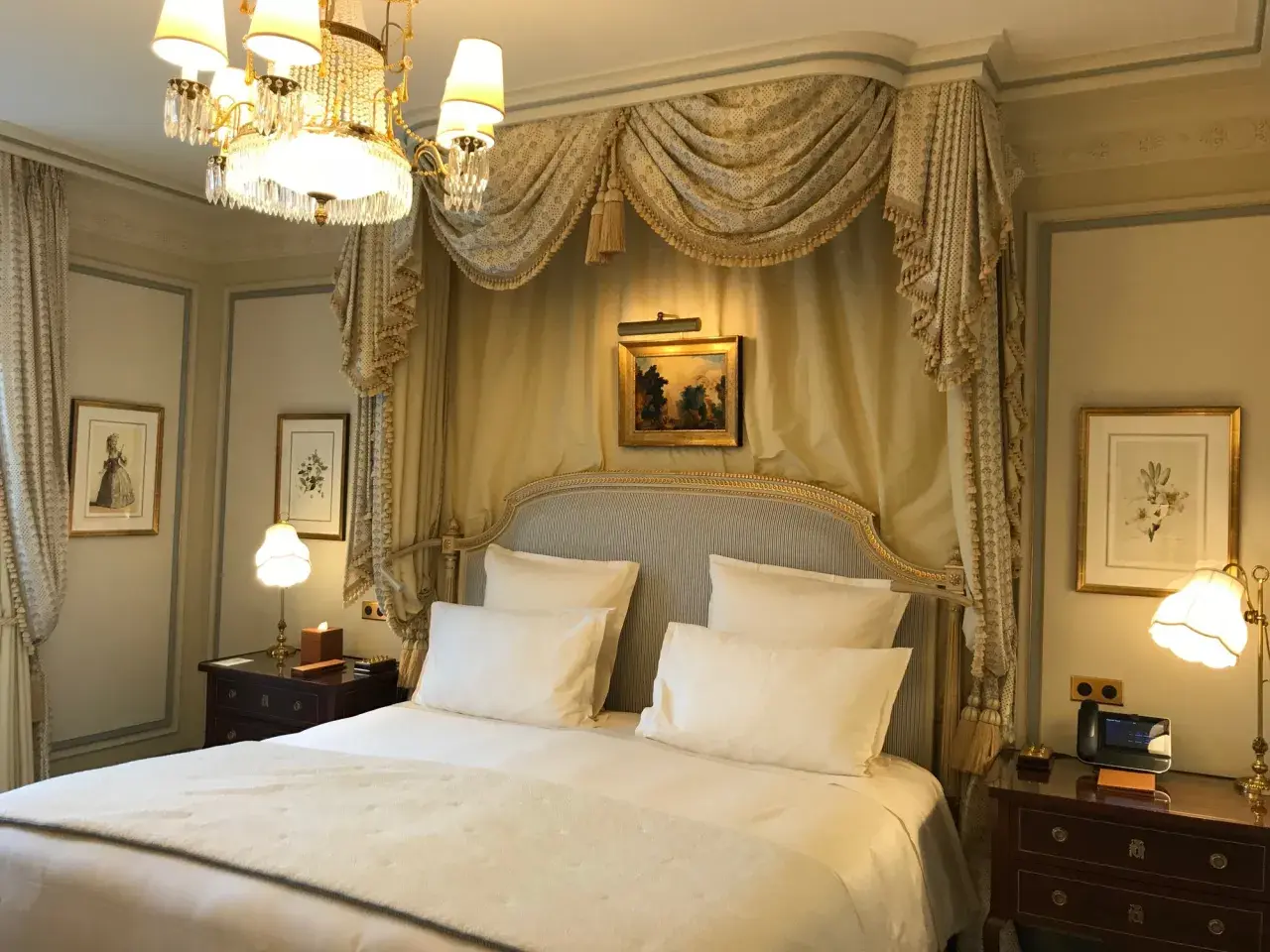 Elegancka sypialnia w hotelu Ritz w Paryżu, z baldachimem nad łóżkiem, kryształowym żyrandolem i zabytkowymi obrazami.