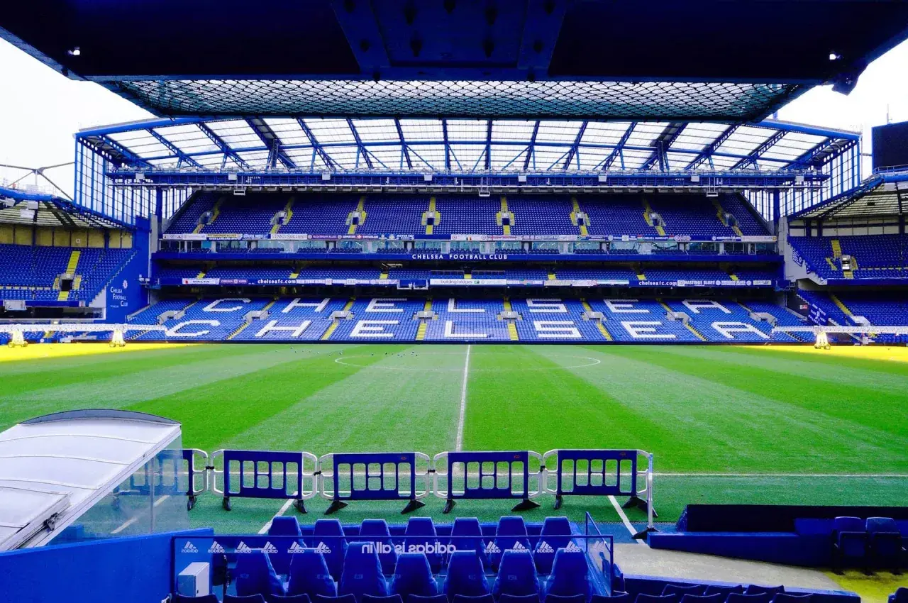 Puste trybuny stadionu Chelsea Londyn, zielona murawa i niebieskie siedzenia czekają na kibiców.