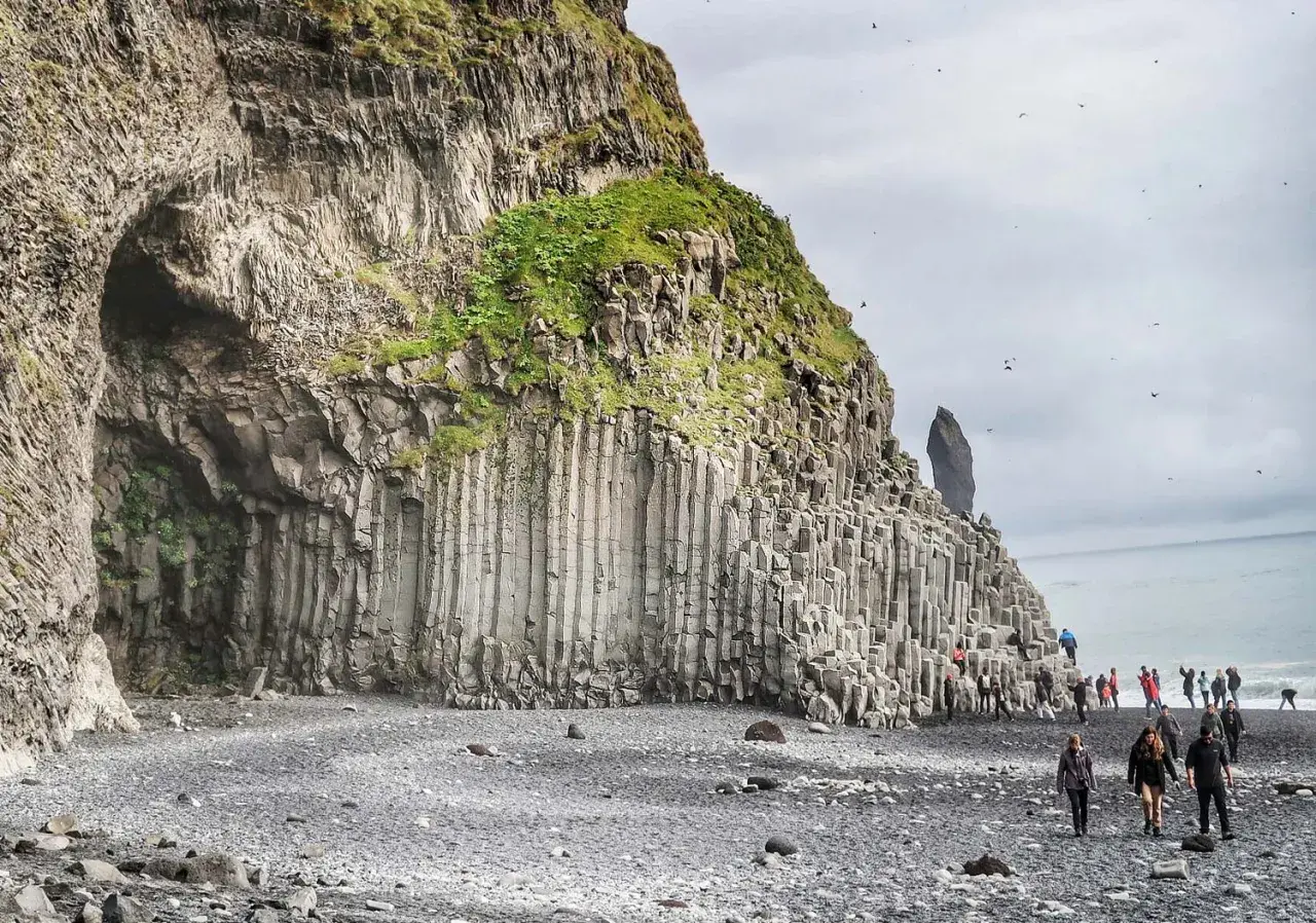 Niesamowita czarna plaża Islandia z bazaltowymi kolumnami i jaskinią. Turyści spacerują po kamieniach.