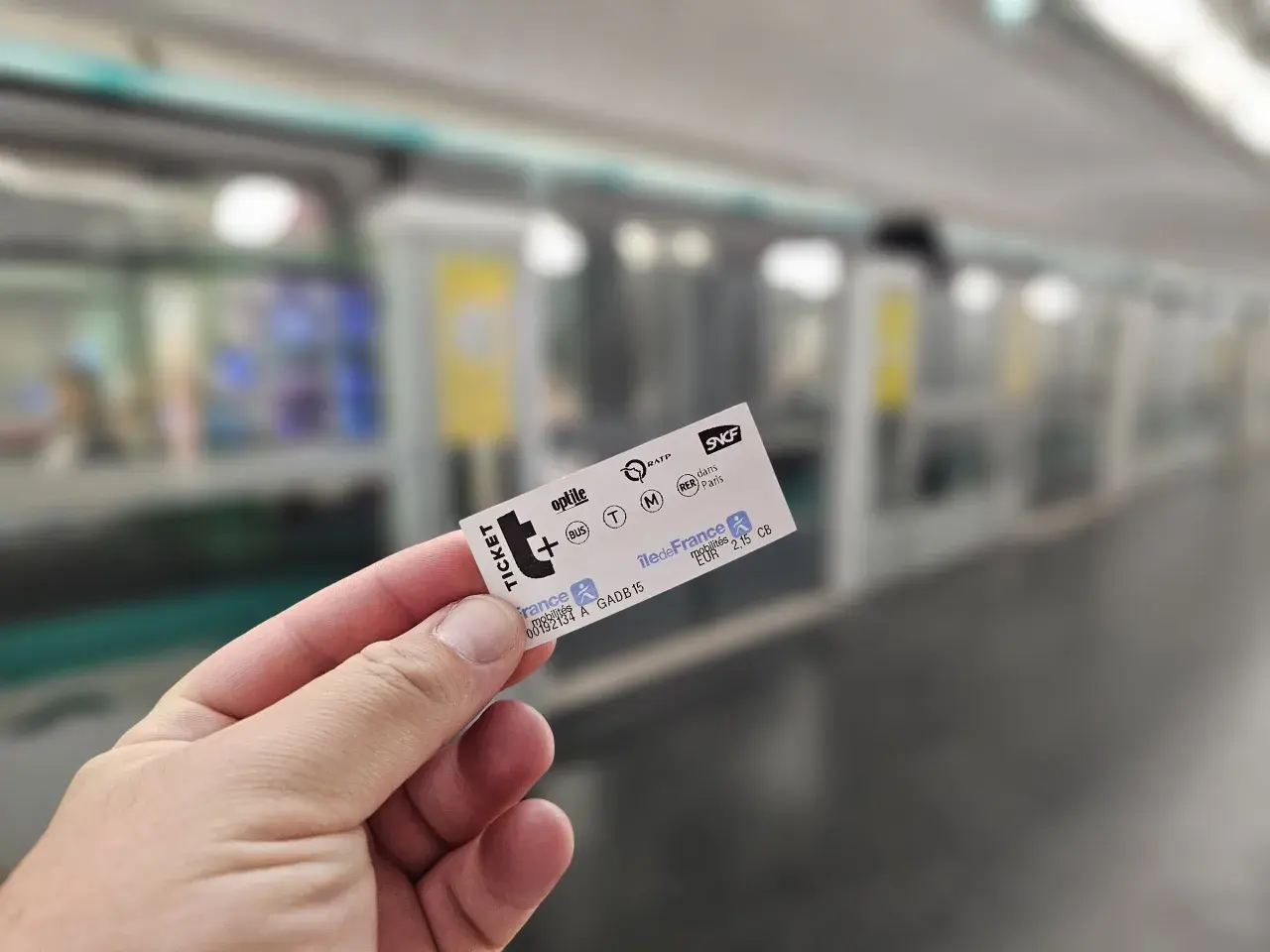Dłoń trzyma bilet metra paryskiego na tle pociągu.