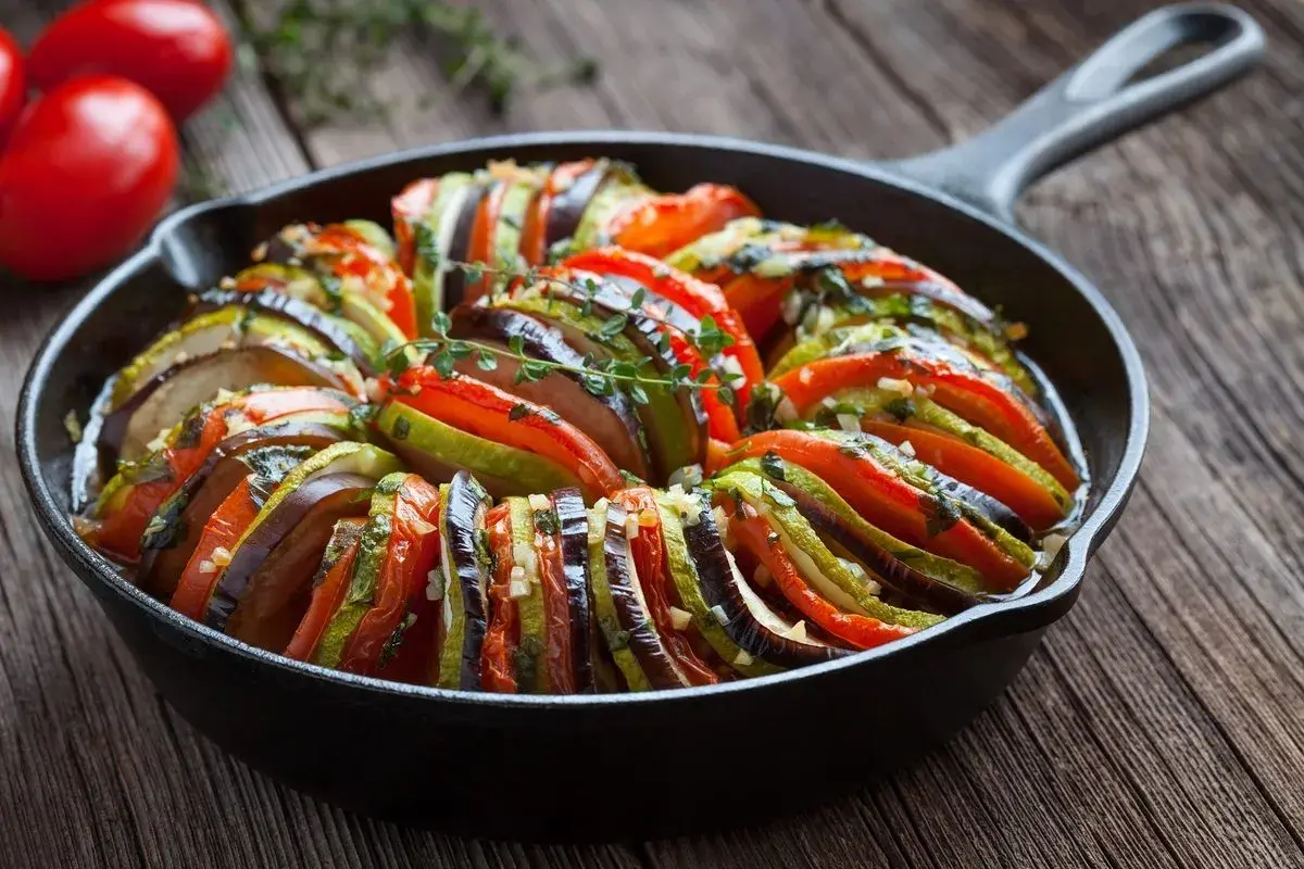 Ratatouille, jedno z popularnych dań francuskich, w naczyniu żeliwnym. Warzywa ułożone w wachlarz, ozdobione ziołami.