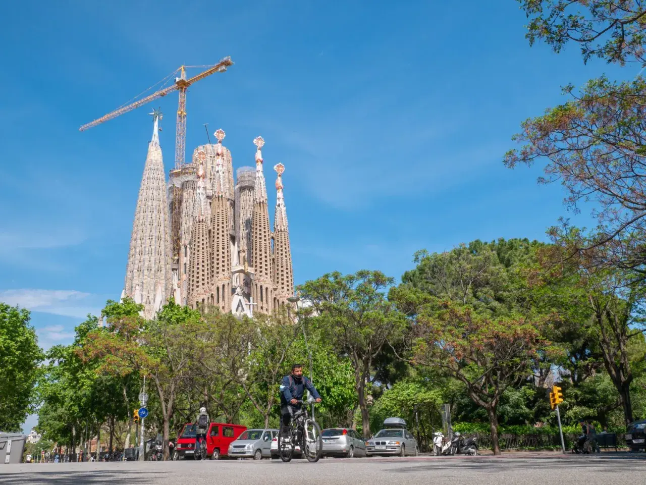 Rowerzysta mija Sagrada Familia, symbol Barcelony, podczas słonecznego dnia. Zwiedzanie tej niezwykłej budowli to marzenie wielu.
