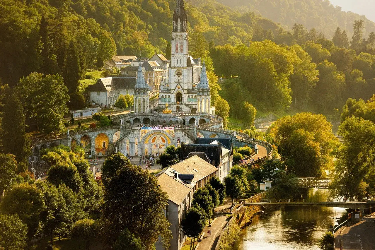 Bazylika w Lourdes, francuskie ośrodek kultu maryjnego, w otoczeniu zielonych wzgórz i rzeki.