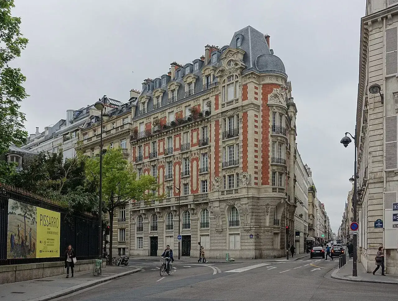 Ulica w Paryżu, z charakterystyczną architekturą. Czy 14 dzielnica Paryża jest bezpieczna? Wygląda na spokojną, z ludźmi spacerującymi i jeżdżącymi na rowerze.