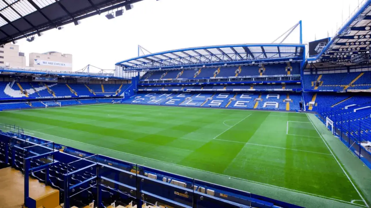 Puste trybuny stadionu Chelsea Londyn, z zieloną murawą i niebieskimi siedzeniami.