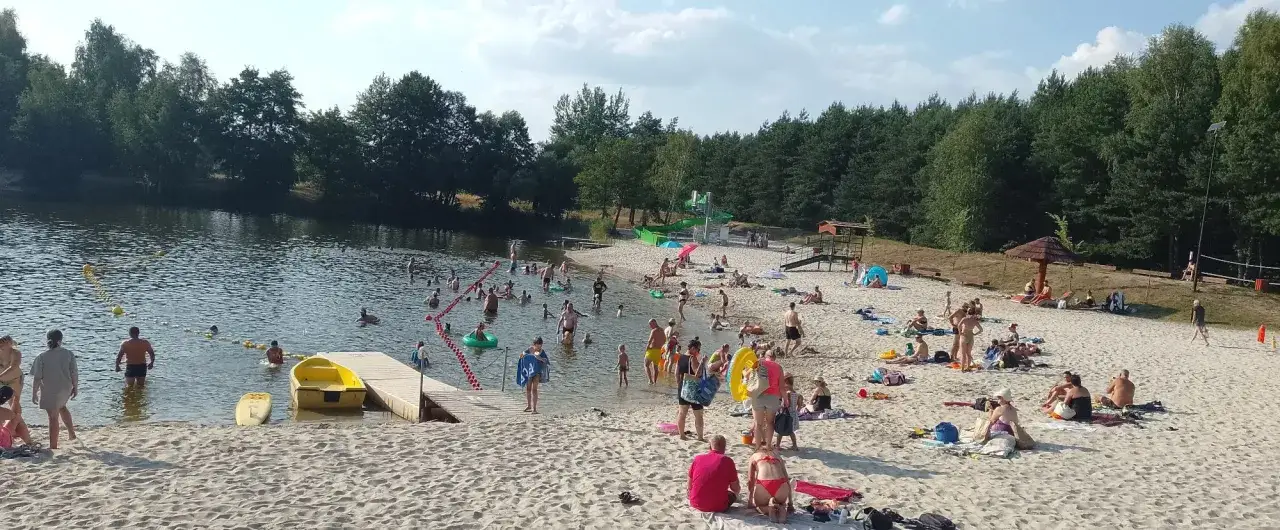 Słoneczna balaton plaża tętni życiem. Ludzie kąpią się, opalają i relaksują na piasku. W tle las.