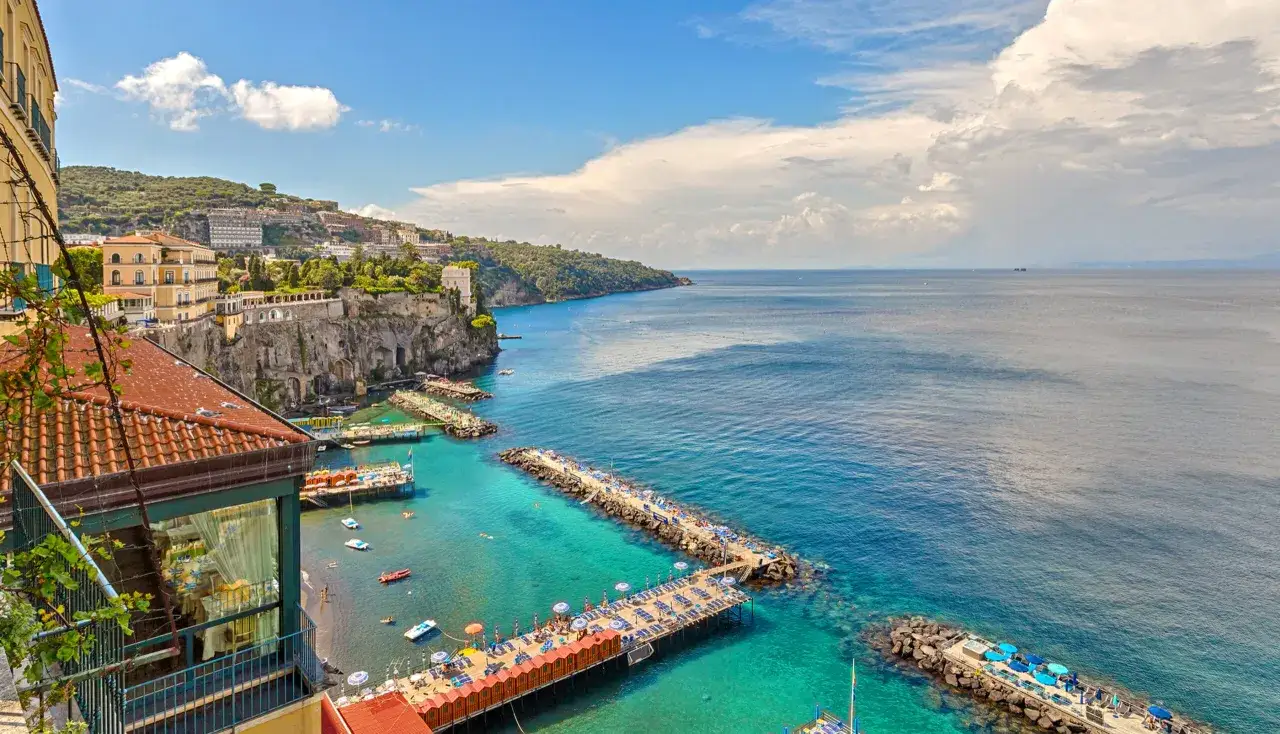 Widok na klify i turkusowe morze w Sorrento. Warto zobaczyć plaże i molo z leżakami.