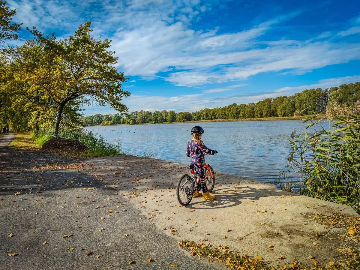Dziecko na rowerze nad jeziorem w bulońskim w Paryżu. Jesienne liście na ścieżce, błękitne niebo z chmurami.