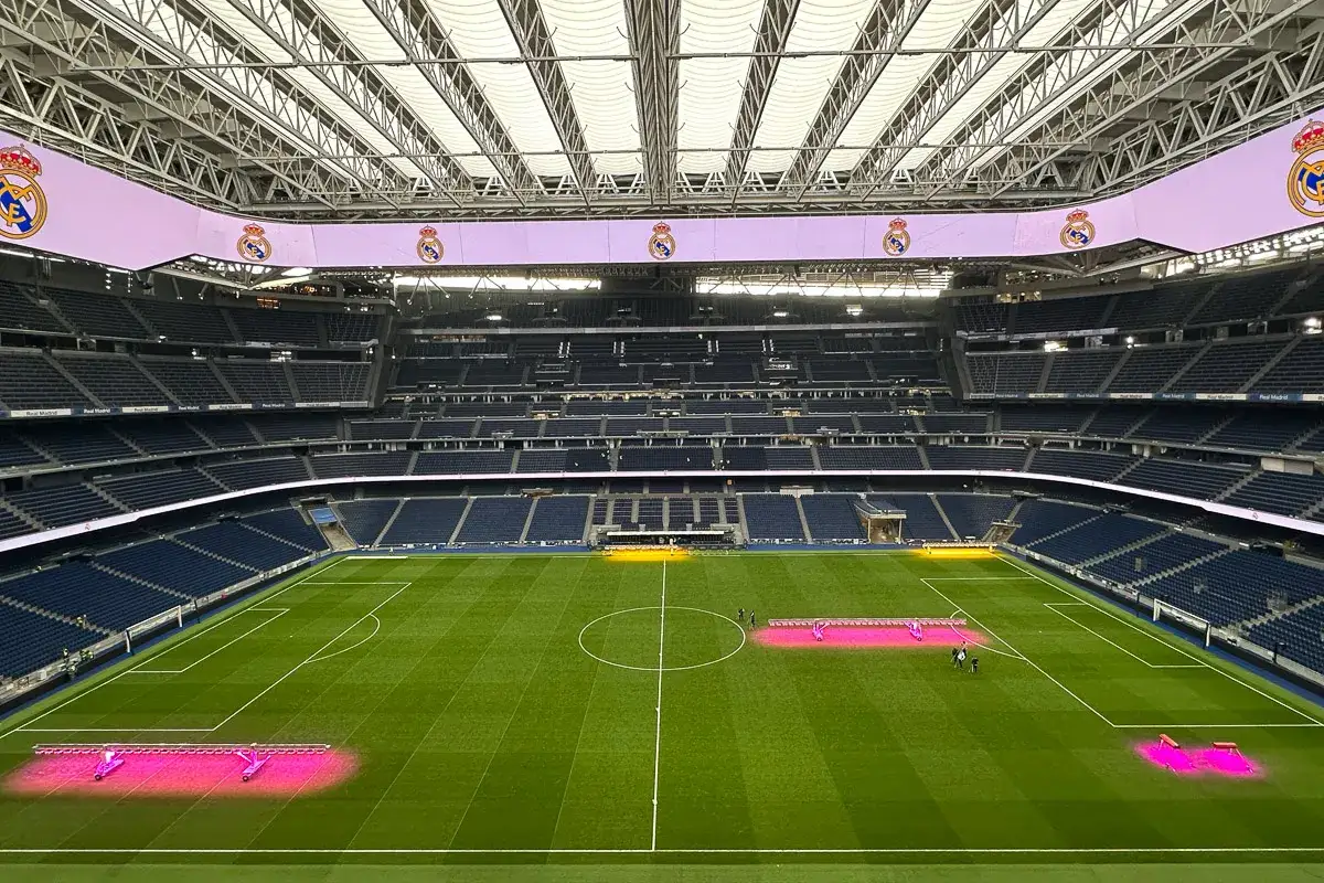 Widok na pusty stadion Santiago Bernabéu podczas zwiedzania. Na murawie widać różowe lampy do pielęgnacji trawy.