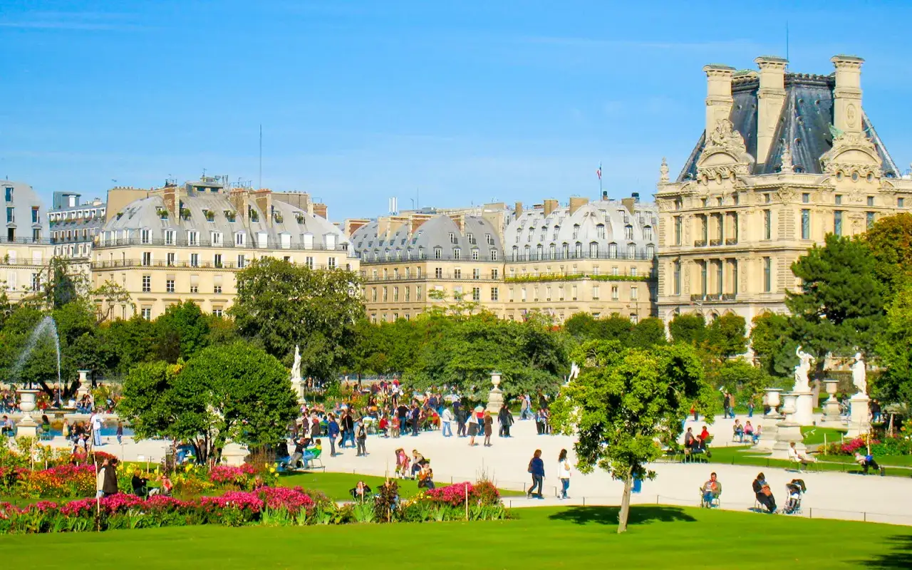 Spacerowicze w 1 dzielnicy Paryża, w Ogrodach Tuileries, podziwiają architekturę i kwitnące kwiaty.