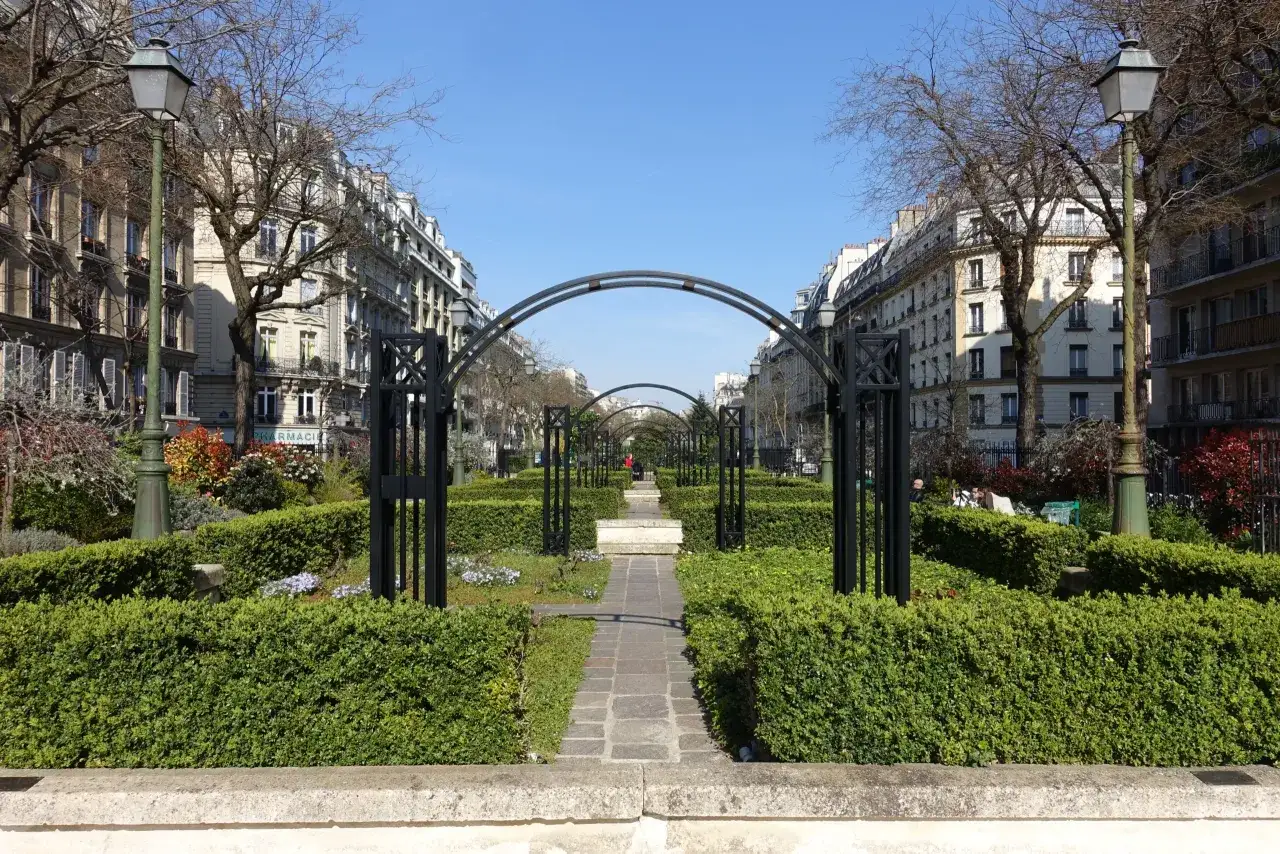 Uroczy park w Paryżu, z zadbanymi żywopłotami i łukami, sugeruje, że 17 dzielnica Paryża jest bezpieczna i przyjemna.