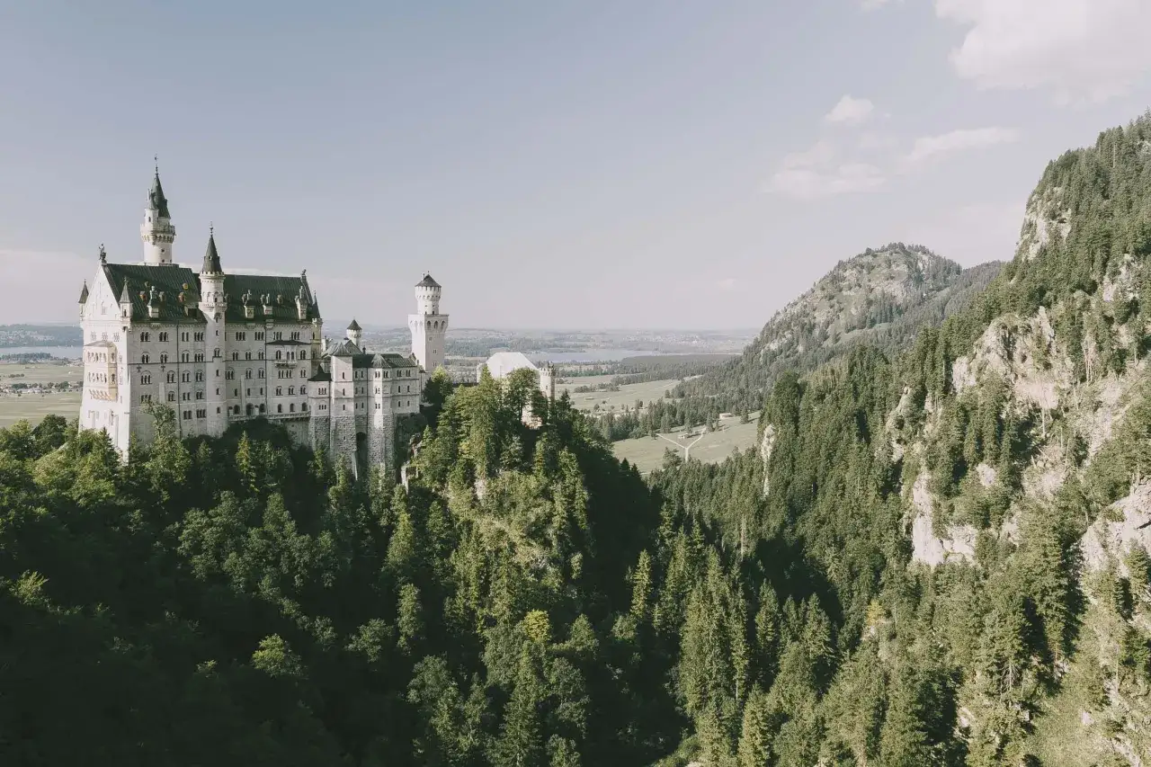 Bajkowy zamek Neuschwanstein, inspiracja dla zamku Disneya w Niemczech, góruje nad zielonymi lasami i doliną.