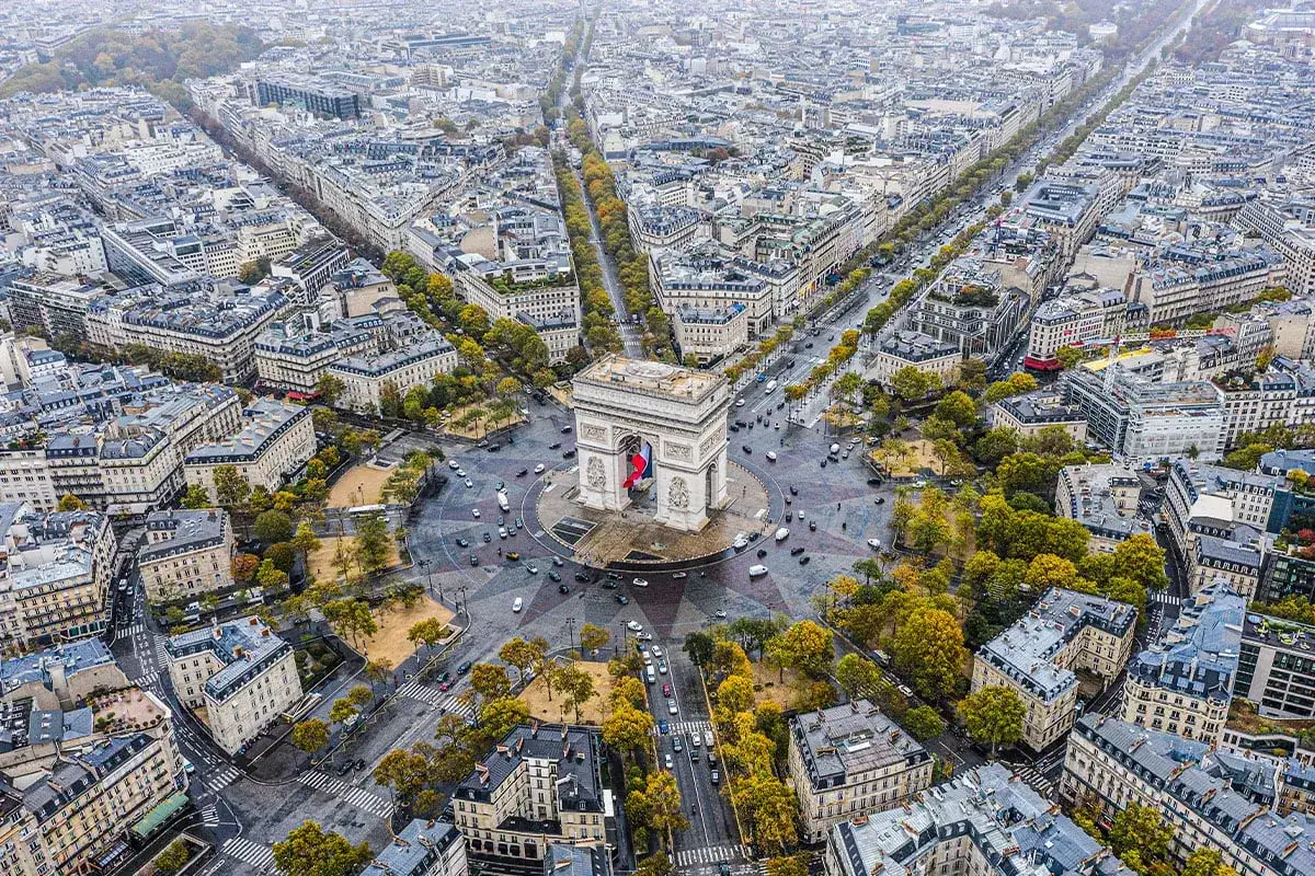Widok z lotu ptaka na Łuk Triumfalny i rozchodzące się od niego aleje, w tym słynne Champs-Élysées, otoczone paryską architekturą i jesiennymi drzewami.
